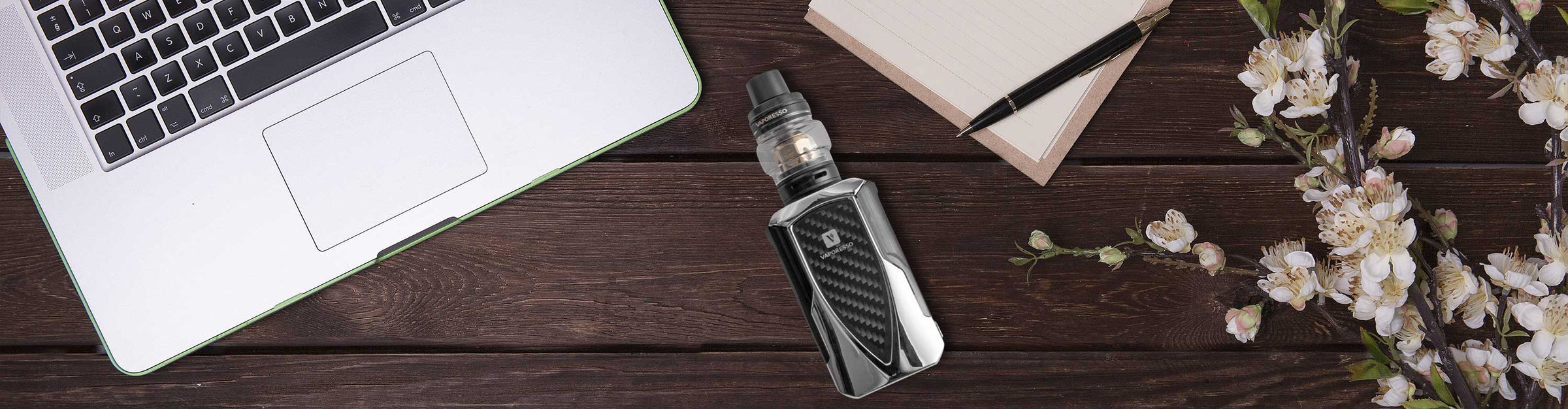 Vaporesso Tarot Vaporizer laying down near laptop and flowers on wooden table.