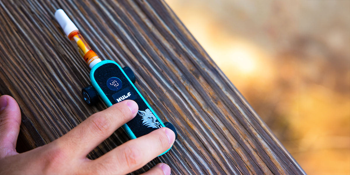 Hand holding a Wulf Deck vape pen on a wooden surface with a blurred natural background
